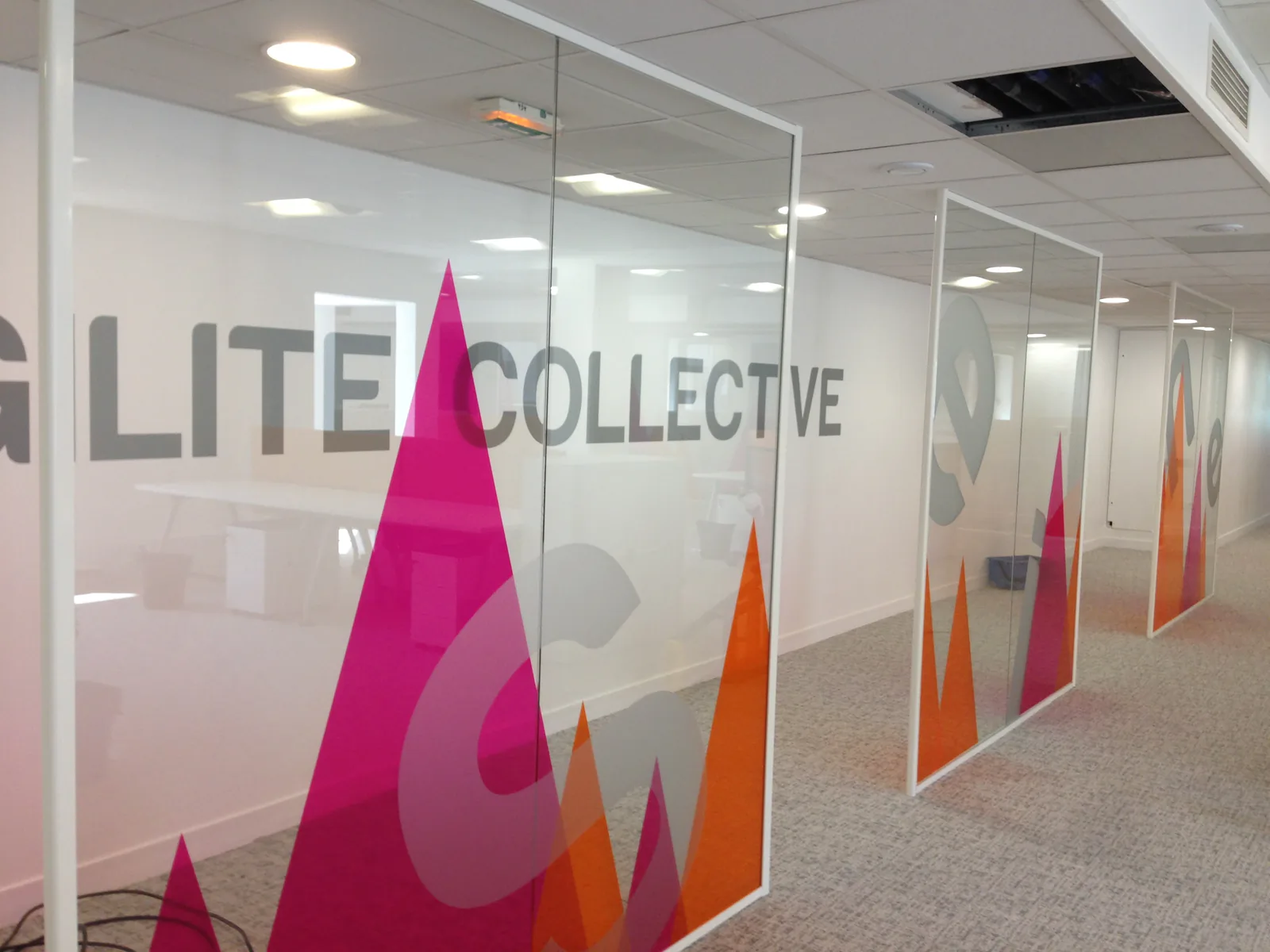 Cloisons vitrées de bureaux avec montagnes graphiques roses et orange et nom d'équipe en lettres adhésives