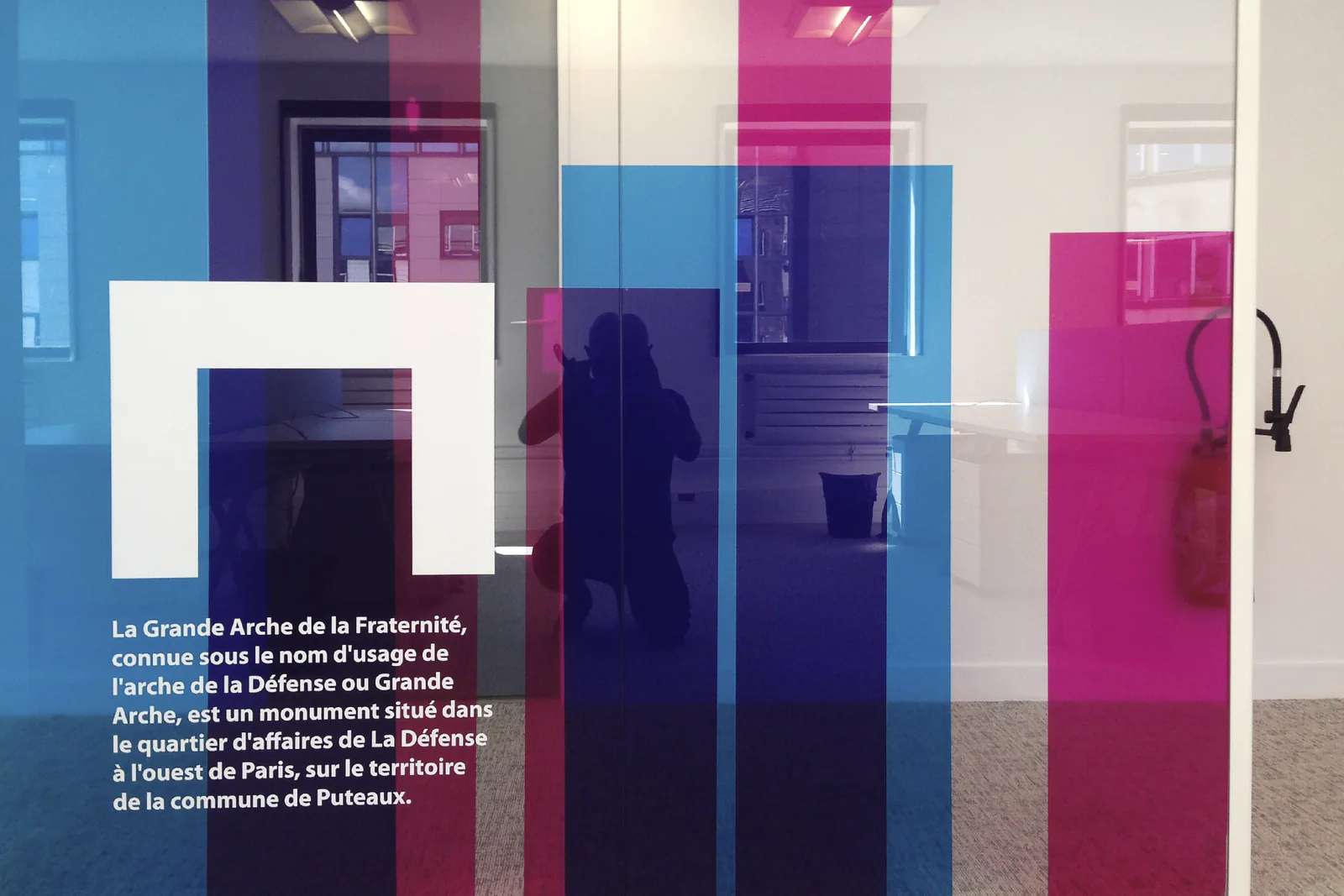 Cloison vitrée avec aplats de couleur translucides et texte adhésif sur la Grande Arche
