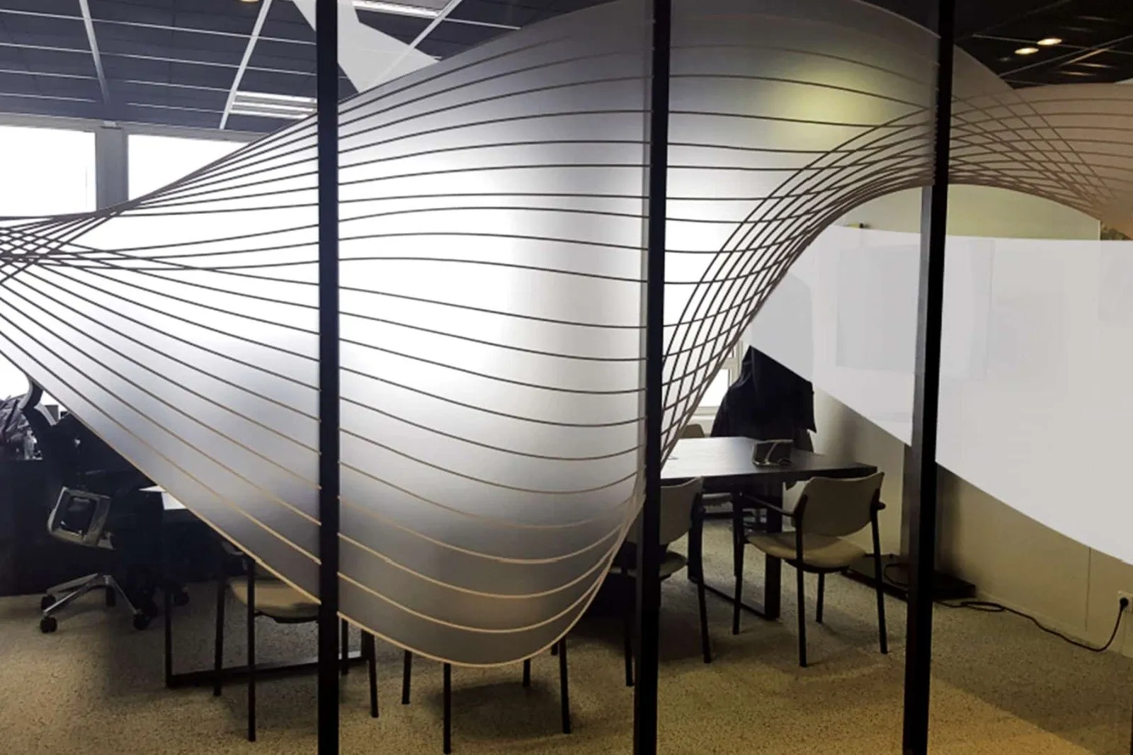 Cloison vitrée de bureaux habillée d'une grande vague de fines lignes en film dépoli qui épouse la courbe de la paroi